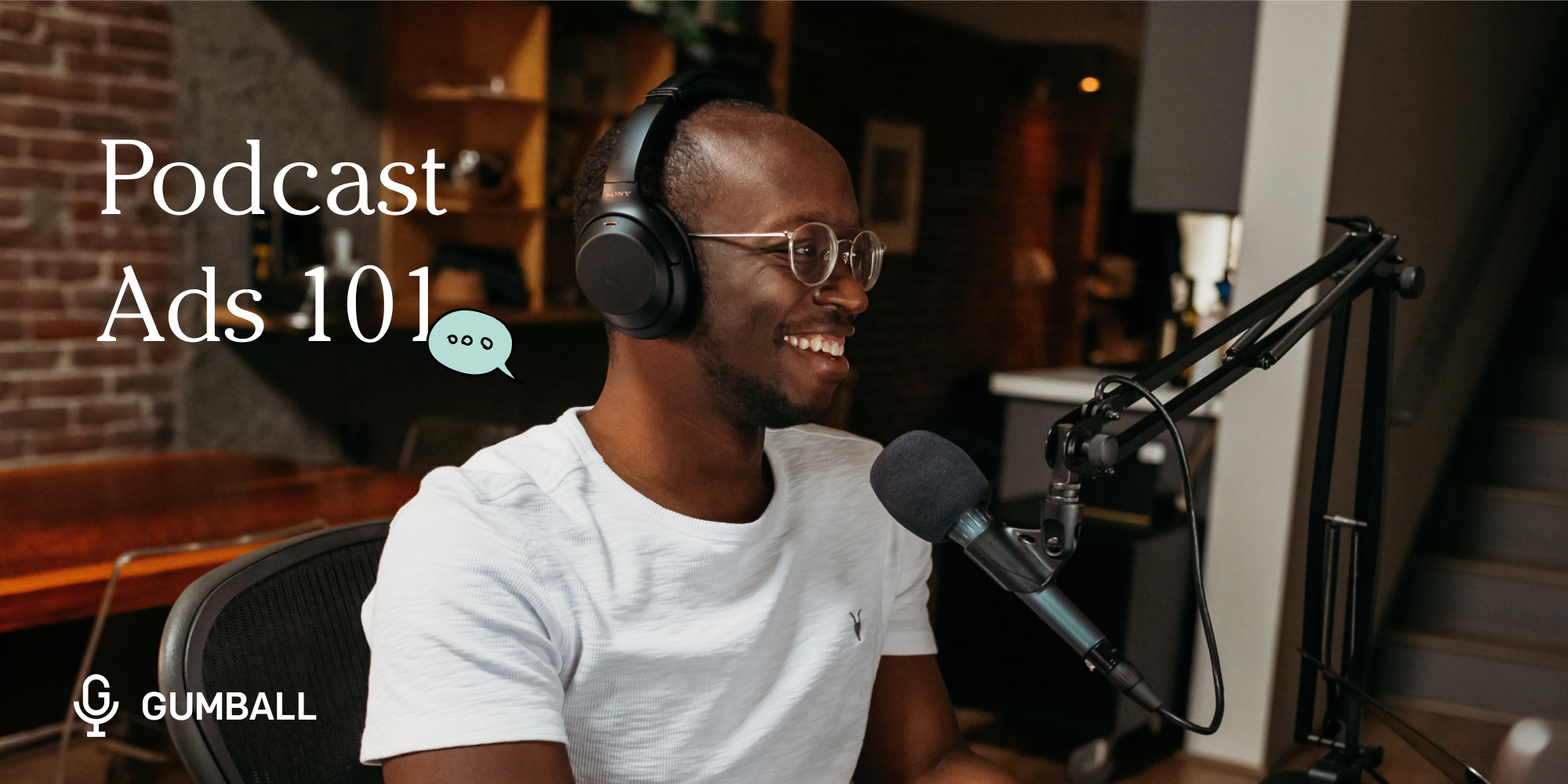 man wearing headphones smiling in front of a podcast mic with the words podcast ads 101 to his left 